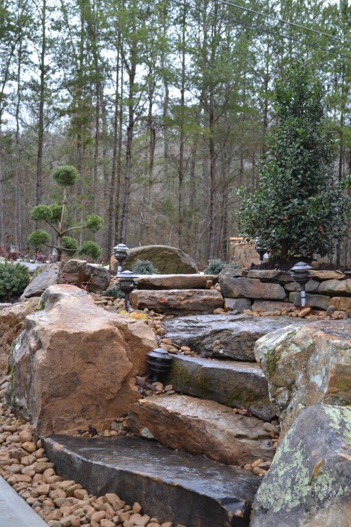 Outdoor Space - Natural stone water feature with cascading stream, boulders, and landscape lighting installation. - Garden Guru Services. Contact Us