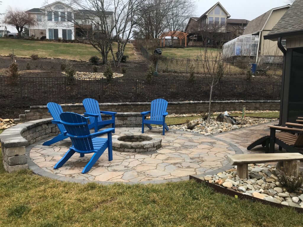 Outdoor Space - Flagstone patio with stone fire pit, retaining wall, and river rock drainage for complete backyard landscape design. - Garden Guru Services