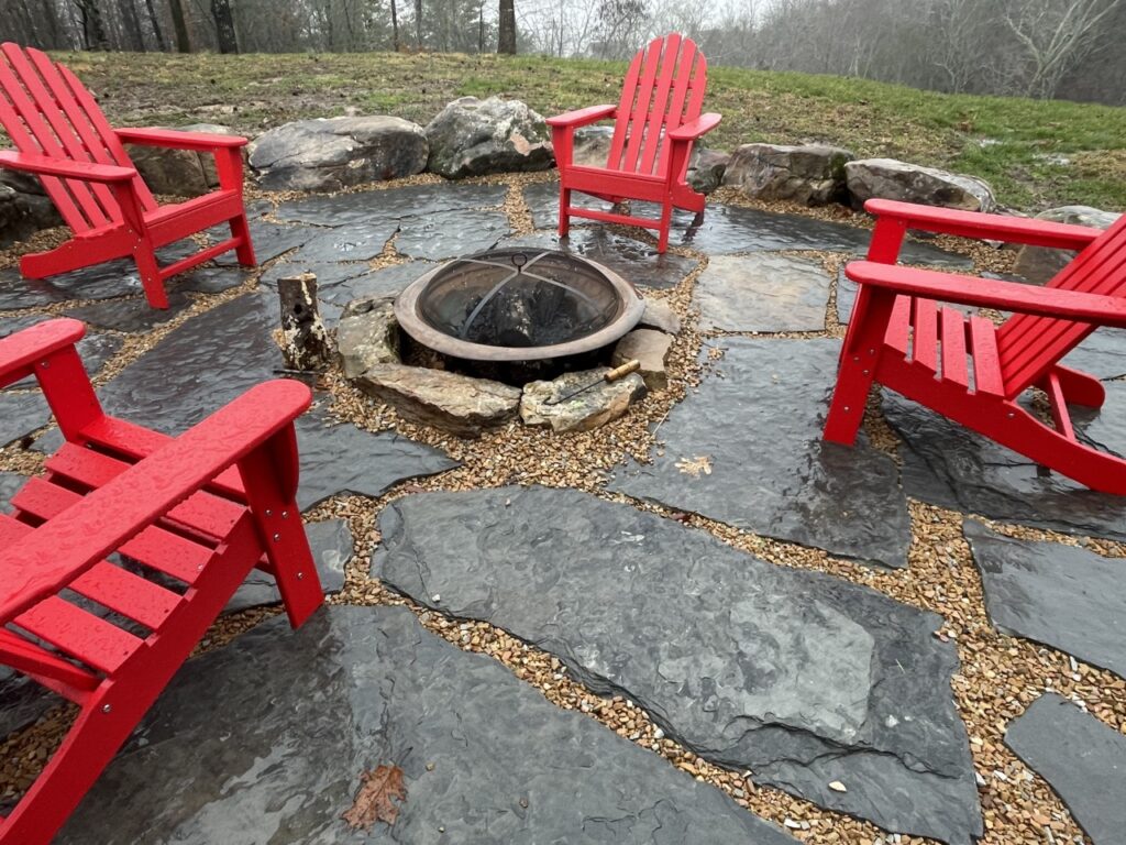 Outdoor Space - Outdoor stone patio with red Adirondack chairs around a fire pit, featuring natural flagstone and gravel landscaping. - Garden Guru Services